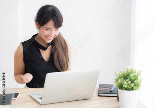 Beautiful portrait asian young woman smile working online laptop computer with happy satisfied sitting on desk office, girl using notebook with excited and glad, business and success concept. © N_studio