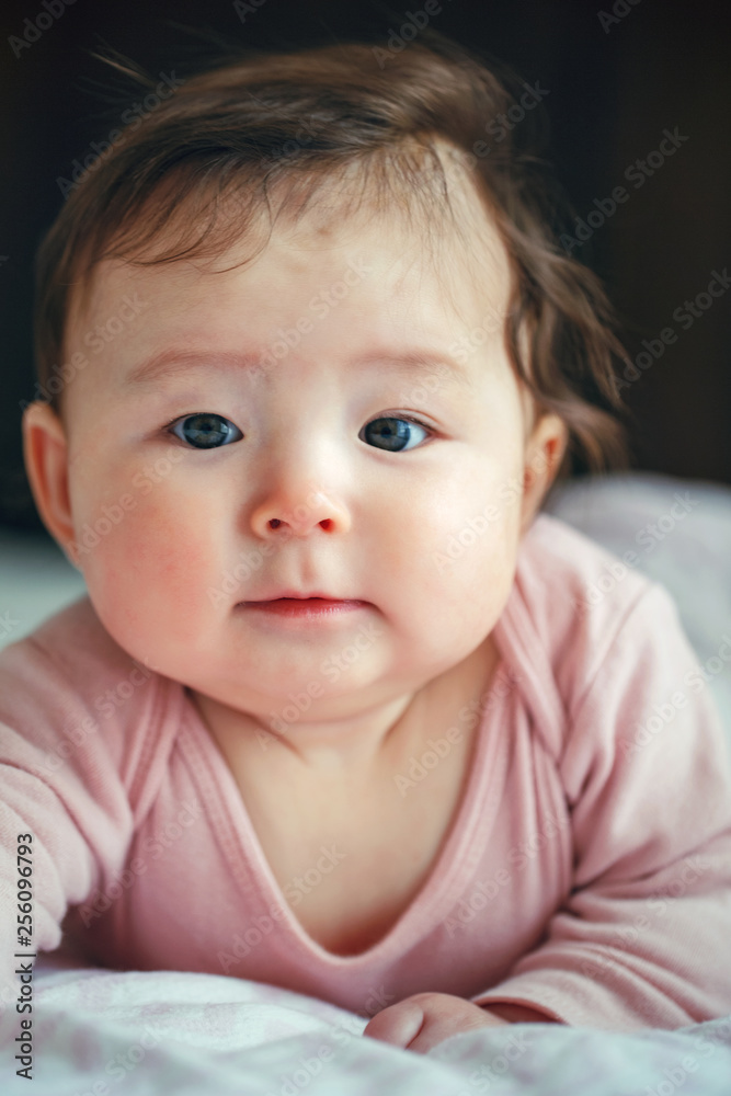 Closeup portrait of cute adorable Asian mixed race baby girl four months old lying on her tummy looking in camera. Natural face expression. Childhood ethnic diversity lifestyle