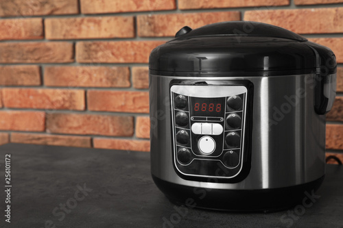 Modern electric multi cooker on table near brick wall. Space for text