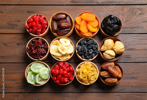 Bowls with different dried fruits on wooden background, flat lay. Healthy lifestyle