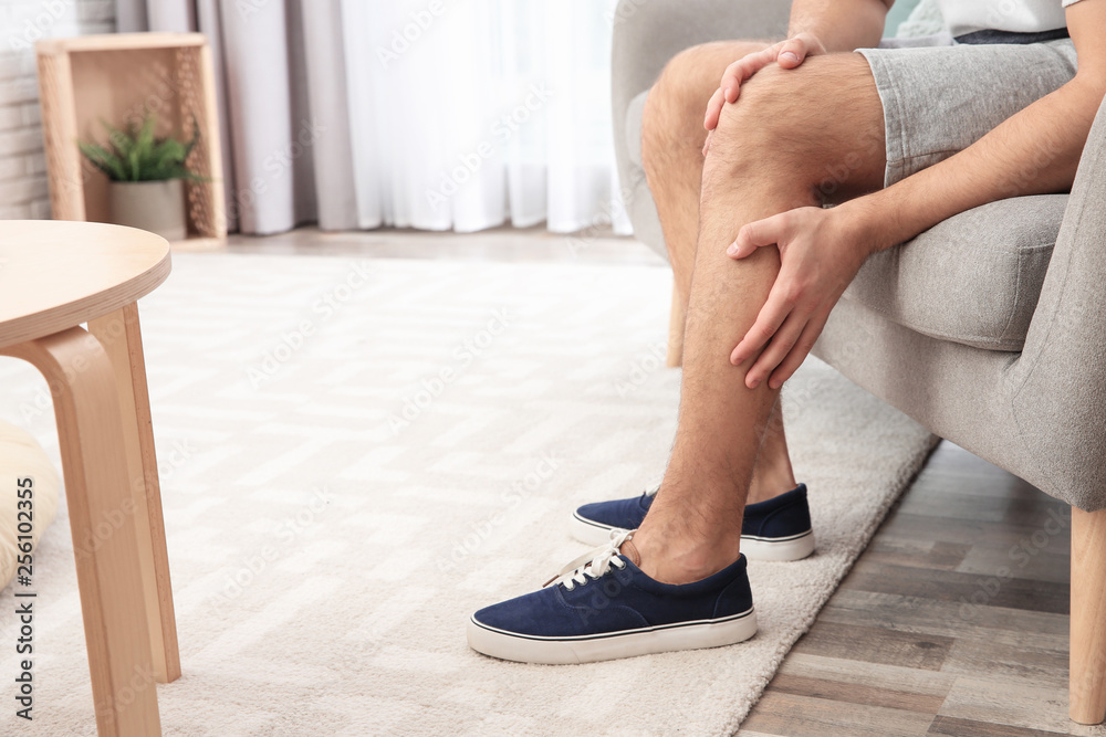 © New Africa - Man suffering from leg pain at home, closeup. Space for text