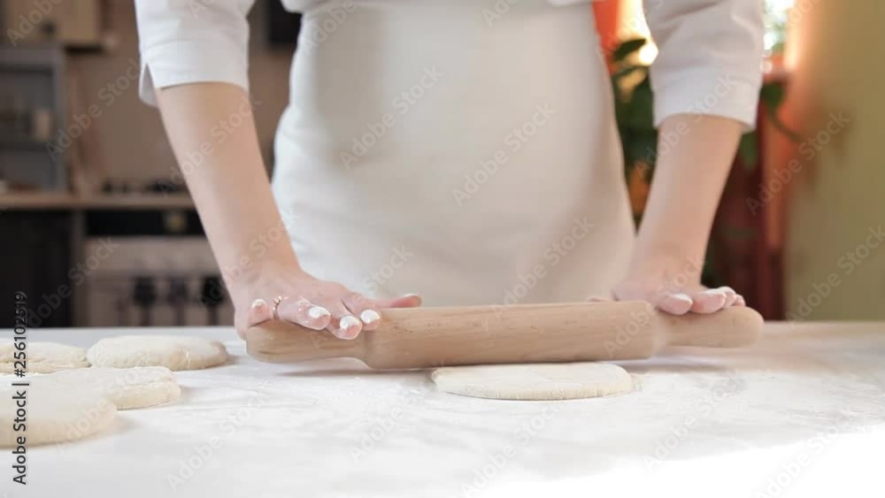 Woman baker rolls the dough with a rolling pin on a background of ingredients on a wooden table and flour Woman baker rolls the dough with a rolling pin on a background of ingredients on a wooden table and flour