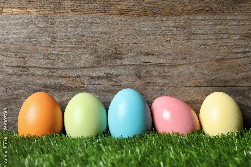 Colorful dyed Easter eggs on green grass against wooden background, space for text