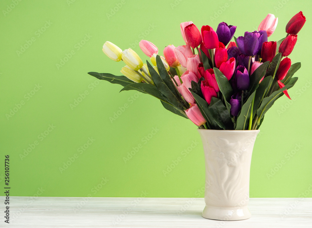 Colorful tulips in vase on white table wall green background