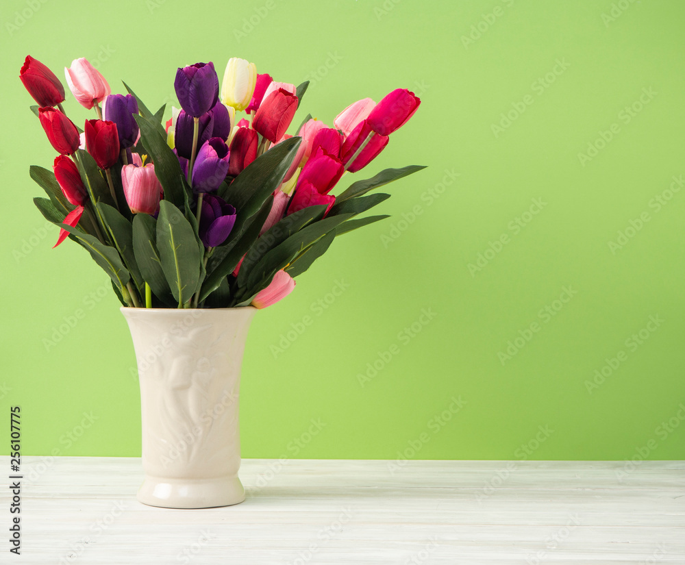 Colorful tulips in vase on white table wall green background Colorful tulips in vase on white table wall green background