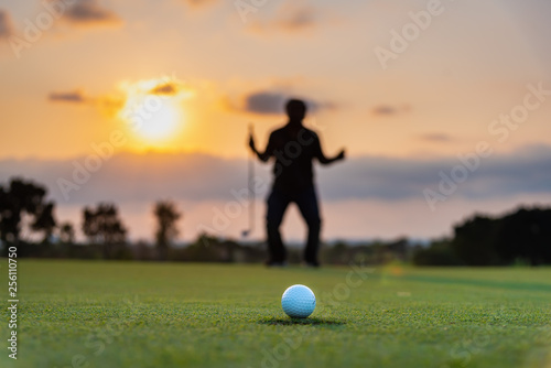 Silhouette golfer showing happiness when win in game , white golf ball on green grass of golf course with blur background.