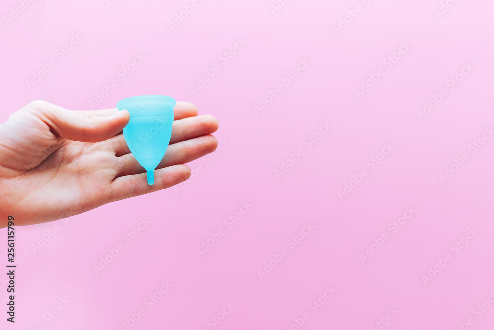 Close up of woman hand holding menstrual cup over pink background. Women health concept, zero waste alternatives Close up of woman hand holding menstrual cup over pink background. Women health concept, zero waste alternatives