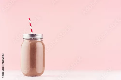 Obraz Słodki czekoladowy koktajl mleczny w staromodnych słoikach ze słomką, srebrną nakrętką na jasnym pastelowym różowym tle.