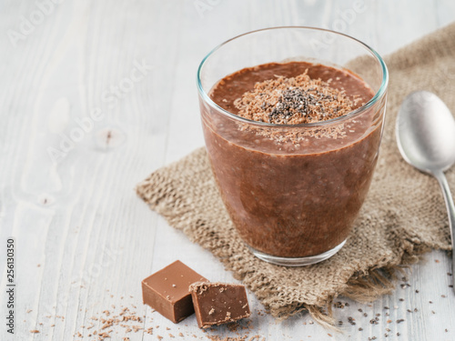 Chocolate chia pudding in glass and chocolate cubes slice with rustic napkin on gray wooden table. Healthy vegan breakfast with copy space. photo