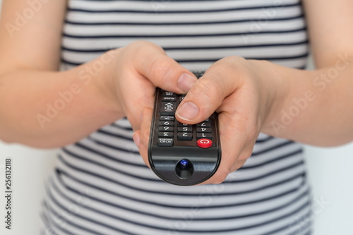Remote control in female hands pointing to TV