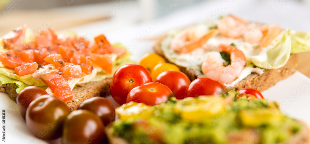 Open sandviches with guacamole, salmon and shrimp and tomato cherry on the plate