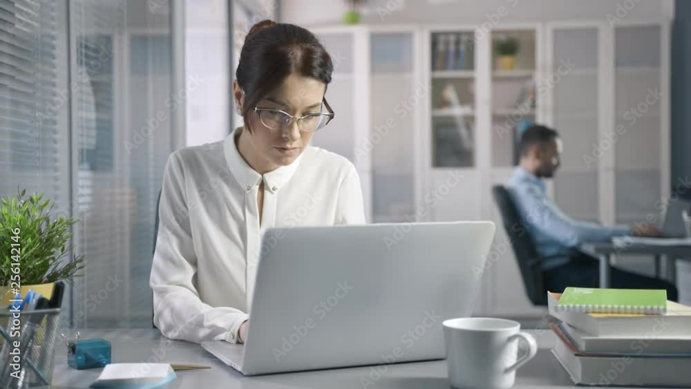 Cute 30s female working at desk in stylish modern sales office using cloud storage. Pretty face Medium Shot with emotion of concentration and success. Student writing a report on successful marketing Cute 30s female working at desk in stylish modern sales office using cloud storage. Pretty face Medium Shot with emotion of concentration and success. Student writing a report on successful marketing
