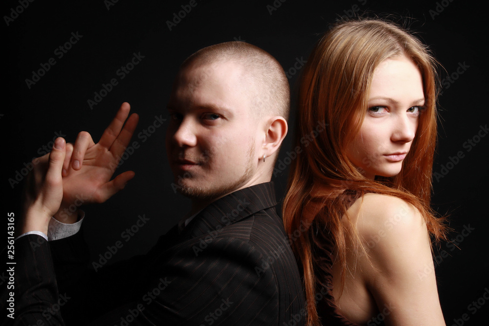 Man in black suit make finger pistol and woman in dress stand back to back playing secret service agent and his lover. Man in black suit make finger pistol and woman in dress stand back to back playing secret service agent and his lover.