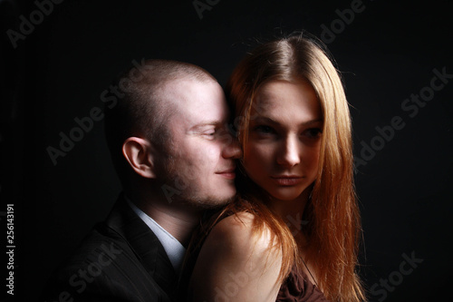 Man hugs his beloved young beautiful woman from behind half-turned.