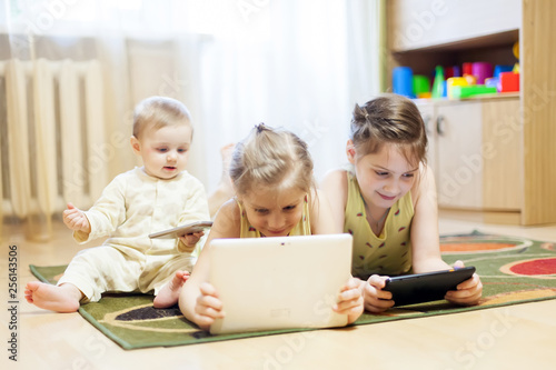 Little baby and older sisters playing tablets and cell phone