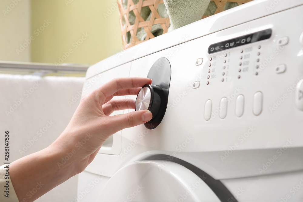 Woman switching on washing machine, closeup Woman switching on washing machine, closeup