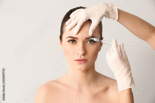 Young woman receiving injection in face on light background