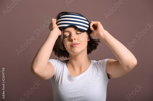 Sleepy young woman with mask on color background