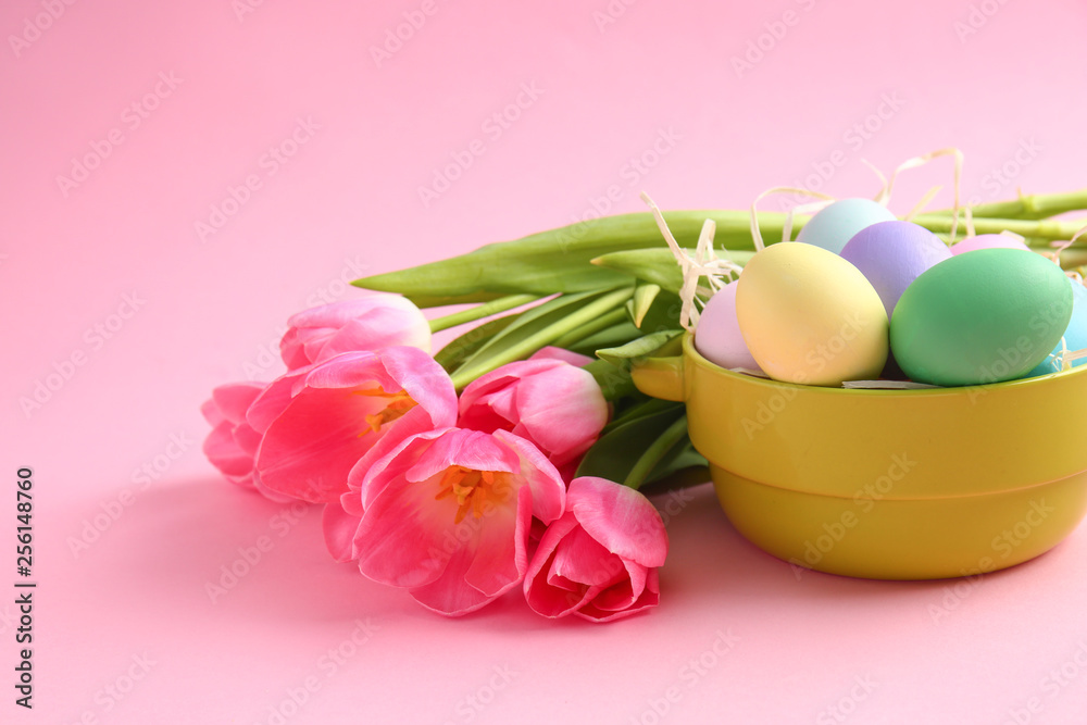Obraz premium Bowl with beautiful Easter eggs and flowers on color background