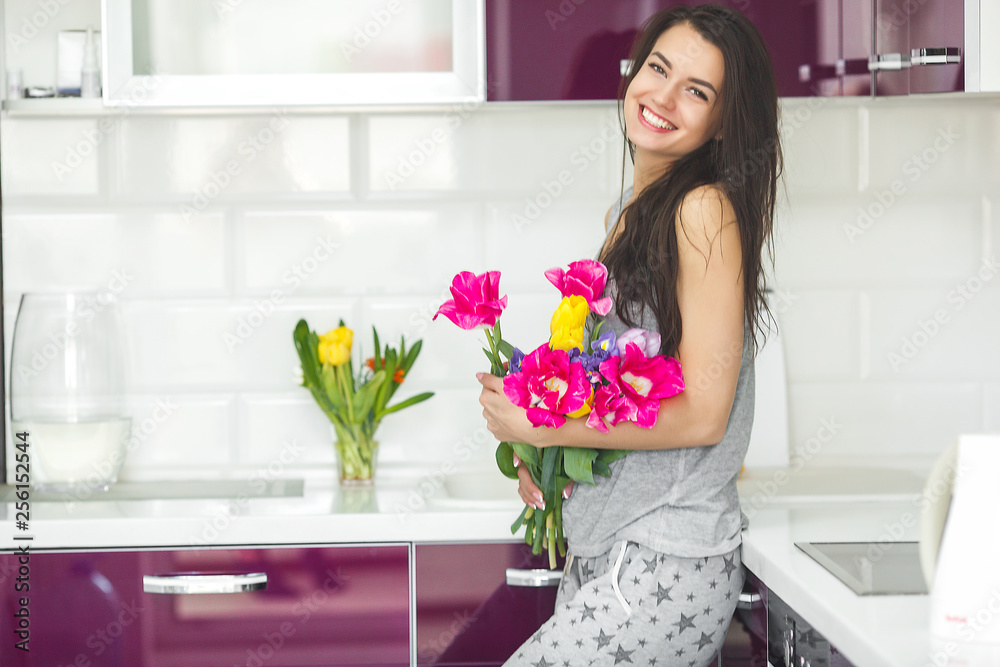 Young attractive woman holding flowers. Lady on the kitchen with tulips. Housewife in the morning standing on the home kitchen. Young attractive woman holding flowers. Lady on the kitchen with tulips. Housewife in the morning standing on the home kitchen.