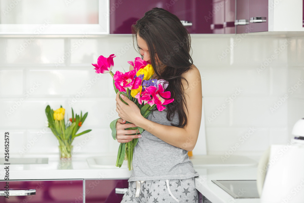 Young attractive woman holding flowers. Lady on the kitchen with tulips. Housewife in the morning standing on the home kitchen. Young attractive woman holding flowers. Lady on the kitchen with tulips. Housewife in the morning standing on the home kitchen.
