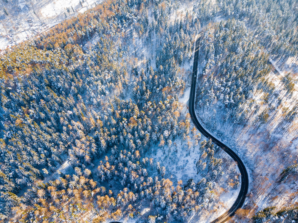 Winding road through the forest, from high mountain pass, in winter time. Aerial view by drone . Romania	