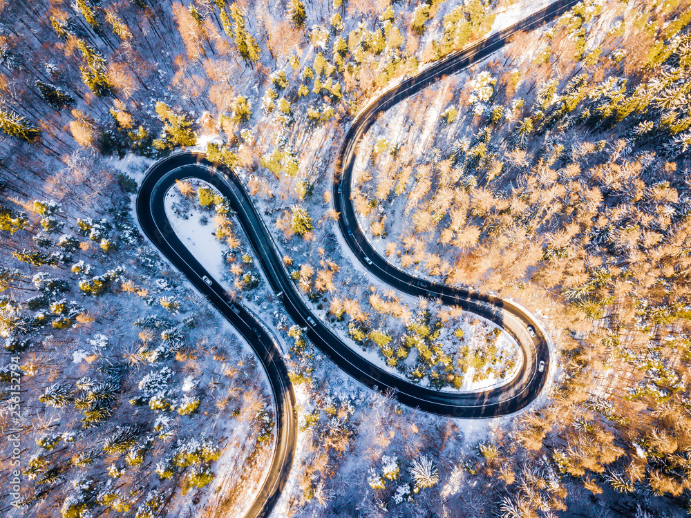 Winding road through the forest, from high mountain pass, in winter time. Aerial view by drone . Romania	