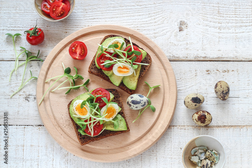 Healthy sandwiches with avocado, tomato, quail eggs and sunflowers micro greens (sprouts) on a white wooden background, flatlay