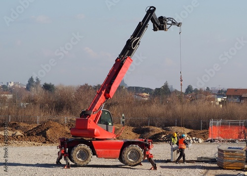 Two workers with a telescopic handler loader assemble concrete slabs for the new building in the construction site. 