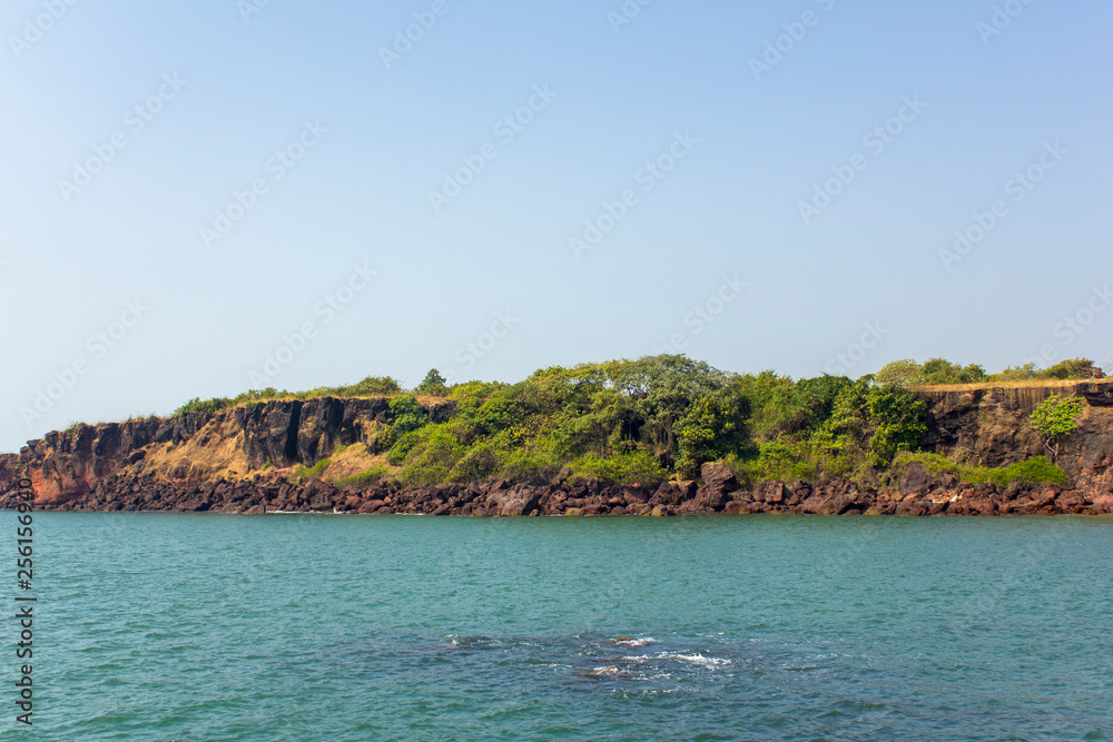 blue ocean on the background of a rocky coast with bright green vegetation under a clear blue sky view from the sea blue ocean on the background of a rocky coast with bright green vegetation under a clear blue sky view from the sea