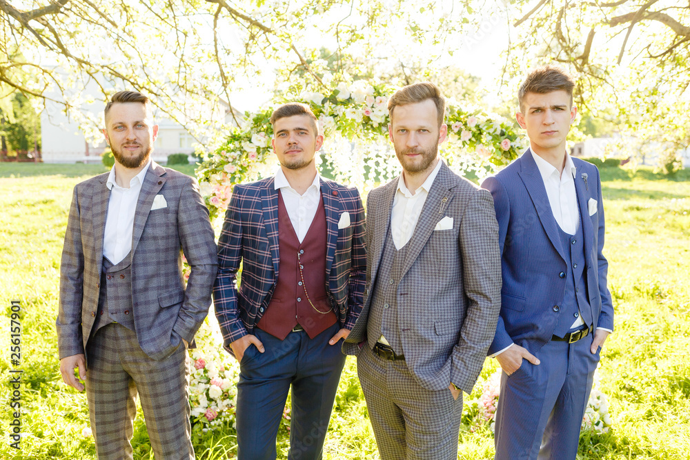 The groom, together with the friends of the groom, is posing against the backdrop of the flower arch at the wedding ceremony The groom, together with the friends of the groom, is posing against the backdrop of the flower arch at the wedding ceremony