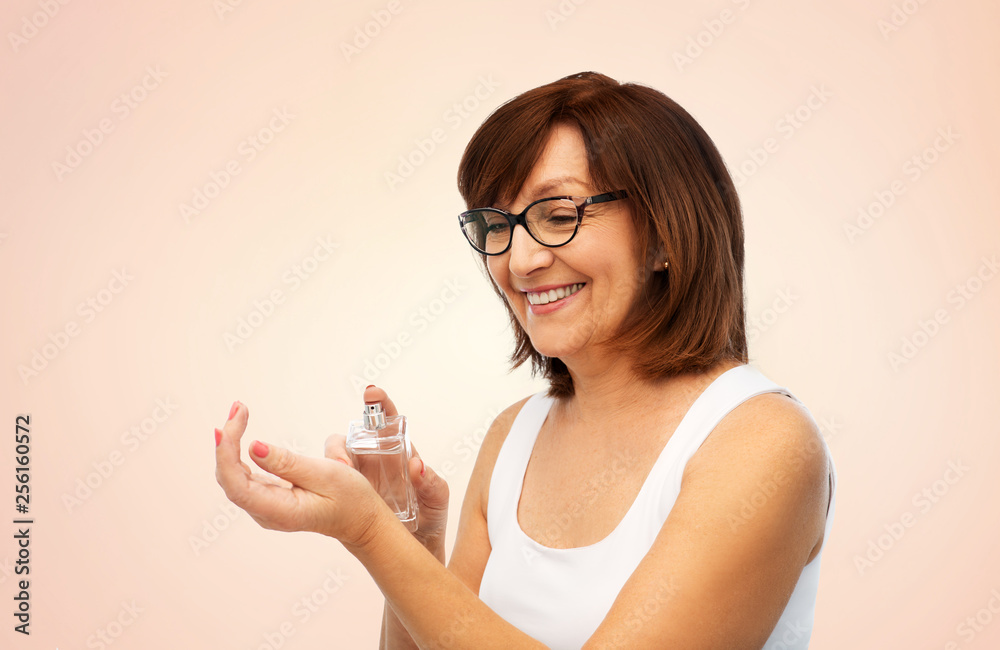 perfumery, beauty and luxury concept - happy smiling senior woman spraying perfume to her wrist over beige background perfumery, beauty and luxury concept - happy smiling senior woman spraying perfume to her wrist over beige background