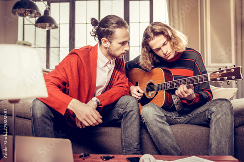 Bearded dark-haired guitar teacher listening to his student