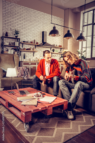 Student wearing jeans and sweater playing the guitar near tutor