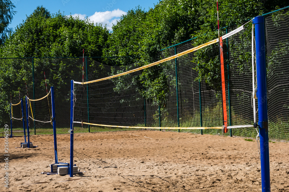 Volleyball net on blue poles on empty sand beach surrounded by lush green trees on summer day