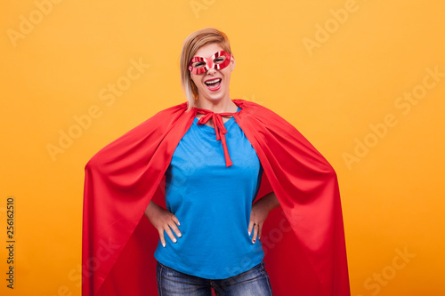 Mother dressed like superheros laughing at the camera over yellow background