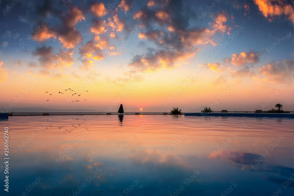 Romantischer Sonnenuntergang mit Spiegelung im Wasser eines Infinity Pools