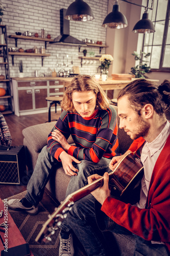 Man striped sweater listening to his friend playing the guitar