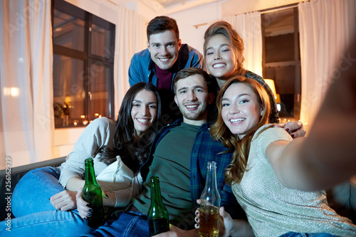 friendship, party and people concept - happy friends with non-alcoholic drinks taking selfie at home in evening