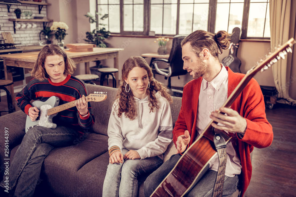 Curly girl looking at her older brother playing the guitar