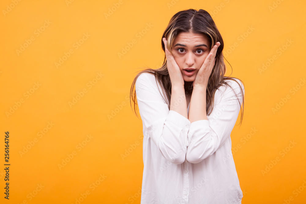 Portrait of a shocked young girl in white shirt over yellow background Portrait of a shocked young girl in white shirt over yellow background