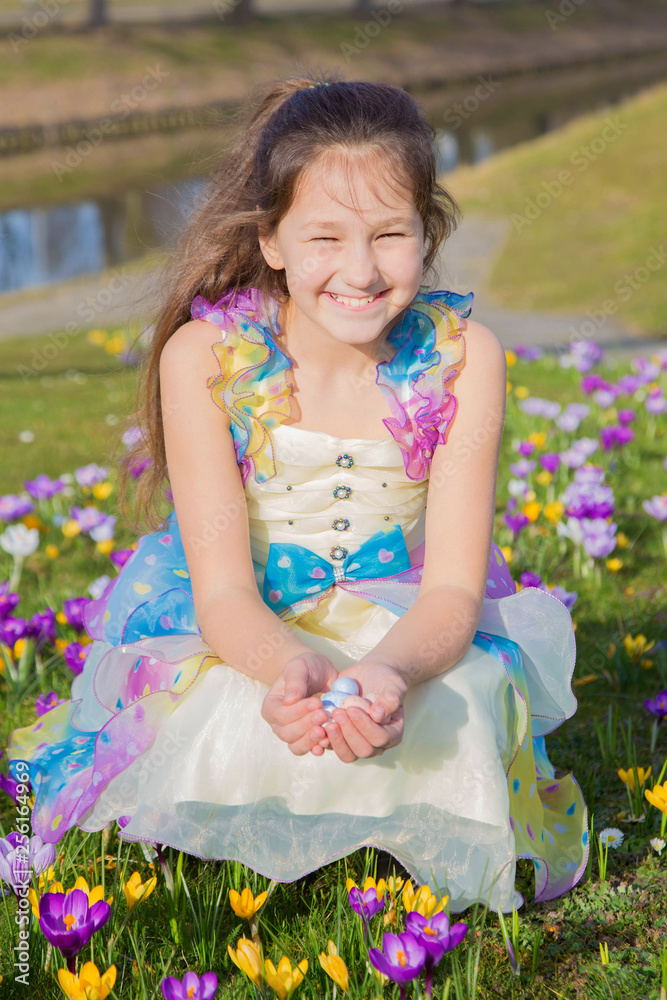 Adorable girl collects Easter chocolate eggs among flowers.