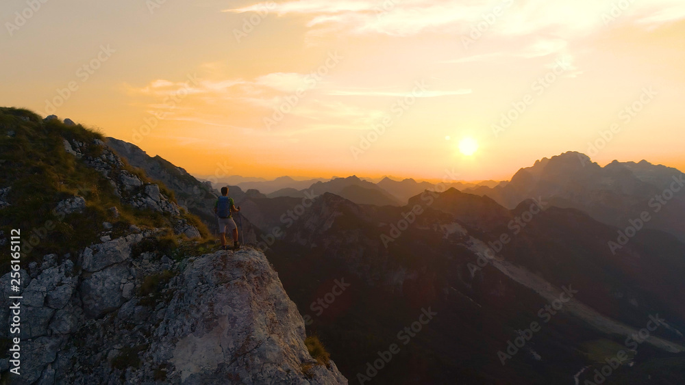 Obraz premium AERIAL Unrecognizable hiker stands on a cliff and observing the golden landscape