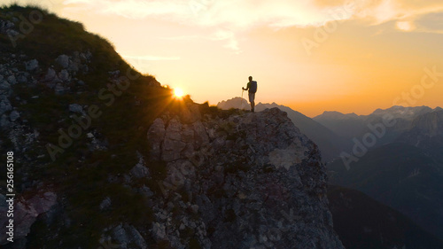 LENS FLARE: Stunning sunset illuminates the Alps and hiker standing on a cliff. © helivideo