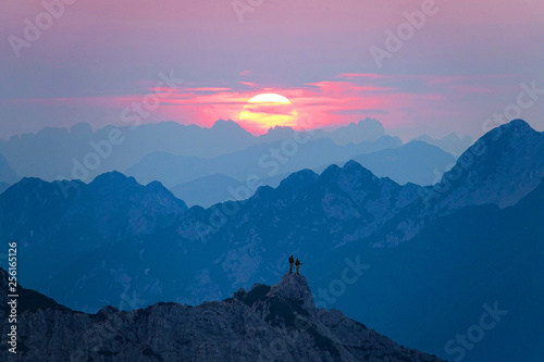 AERIAL: Hiker couple stands on a rocky mountain peak and watch the sunrise.