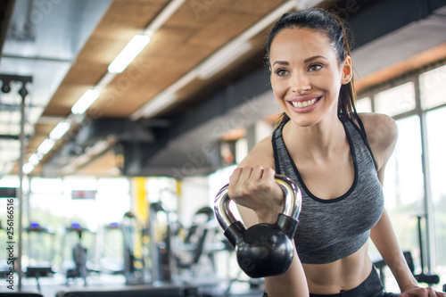 Smiling young woman working out with kettle bell in gym