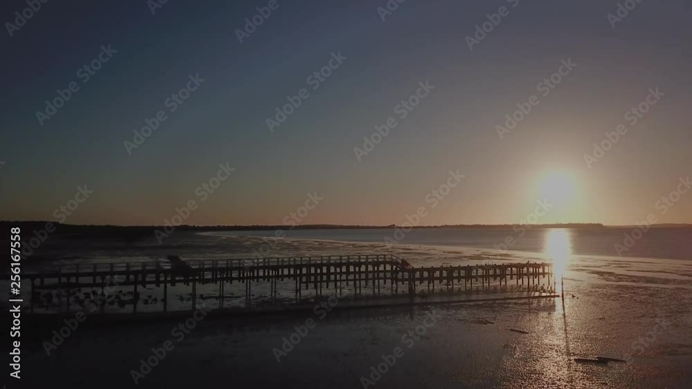 Aerial drone flight towards a pier or jetty during sunset at low tide. Aerial drone flight towards a pier or jetty during sunset at low tide.