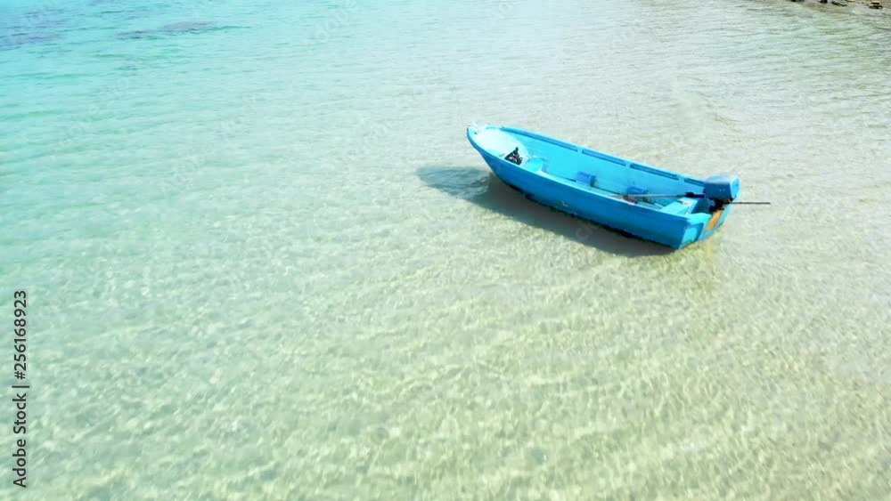 Flying over blue rowing boat tied on shore of exotic beach. Flying over blue rowing boat tied on shore of exotic beach.
