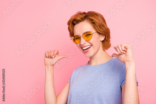 Close-up portrait of her she nice cute charming attractive lovely cheerful cheery girl wearing casual blue t-shirt yellow glasses pointing at herself thumbs isolated over pink background