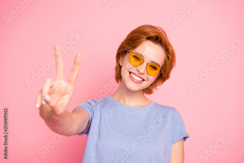 Close-up portrait of her she nice cute charming attractive lovely winsome cheerful optimistic girl wearing casual blue t-shirt yellow glasses giving you v-sign isolated over pink background